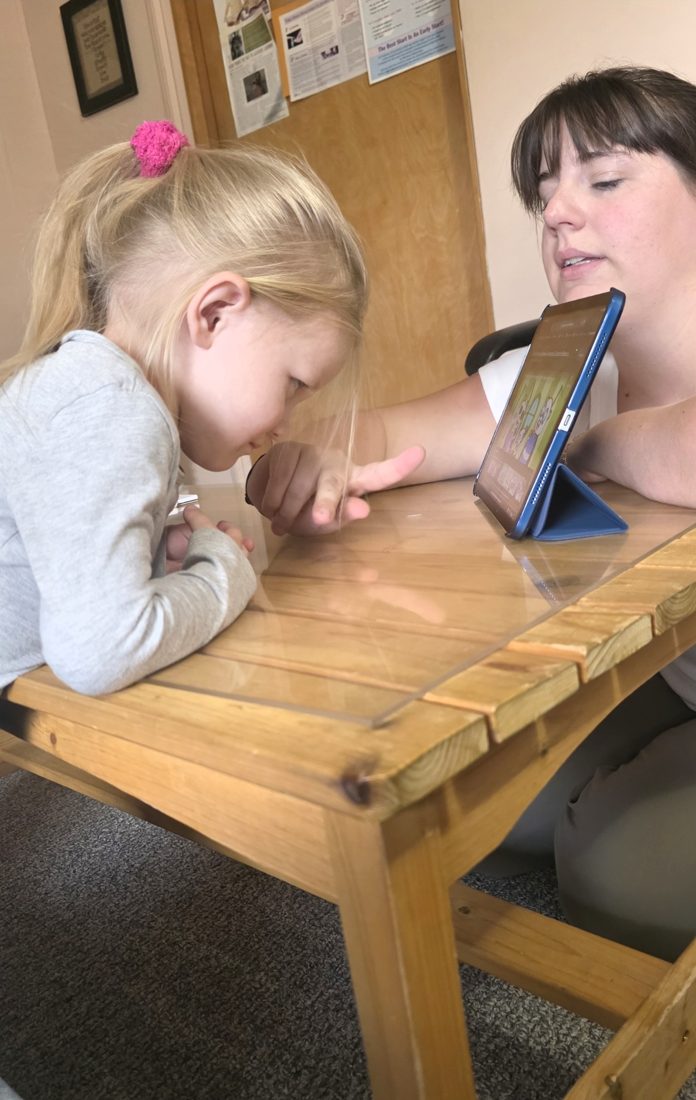 A speech-language pathologist and a young child looking at a tablet together at a table